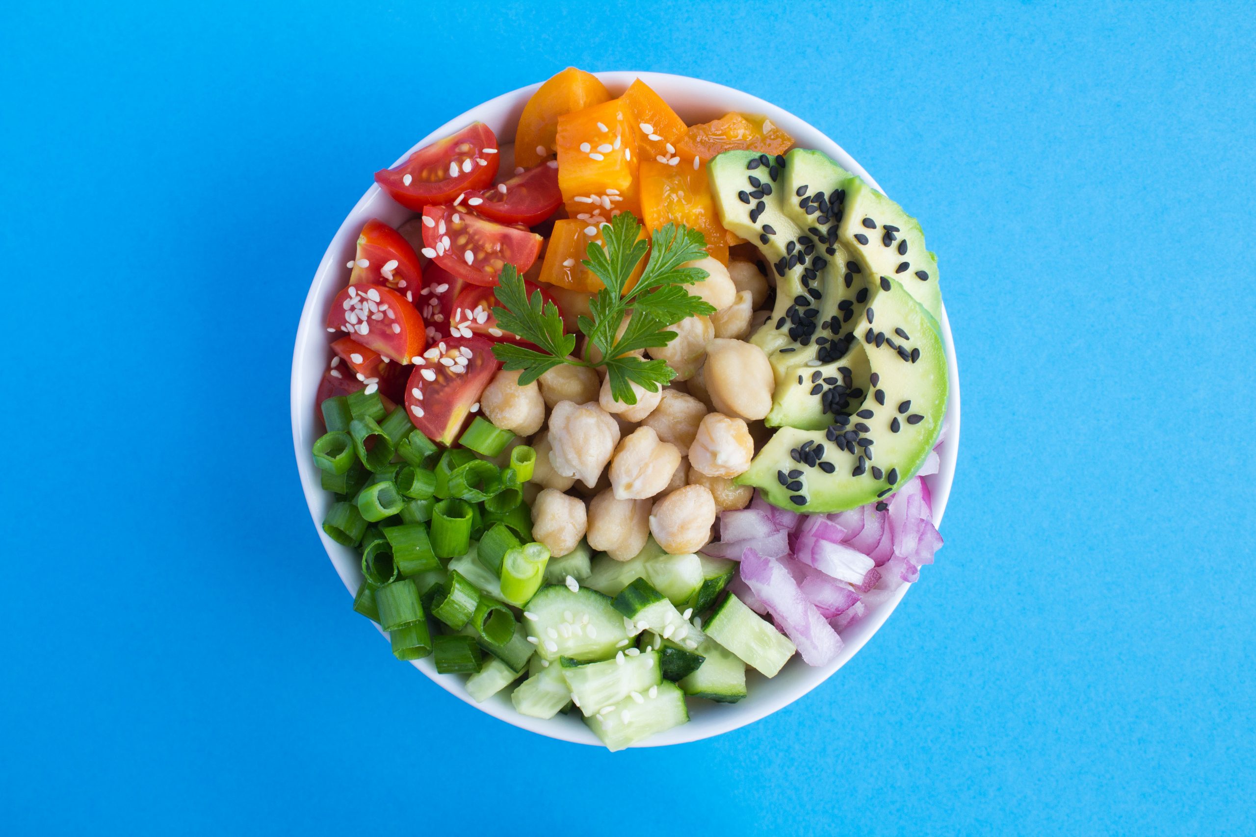 Vegan poke bowl with chickpea  and vegetables in the white bowl in the center of the blue  background.Top view.Closeup.