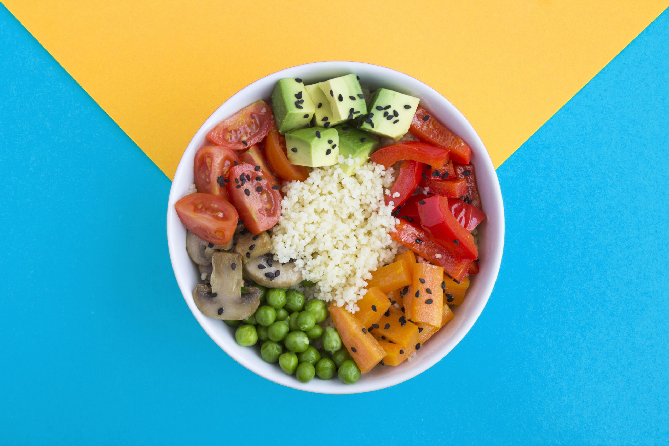Vegan poke bowl with couscous  and vegetables in the white bowl in the center of the bicolor background. Top view. Copy space. Closeup.